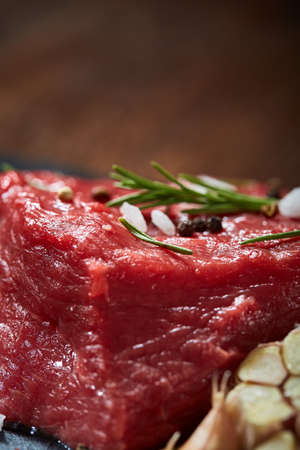 Raw meat beef steaks on black slate board with spices, garlic and rosemary over wooden background, copy space, selective focus, shallow depth of field. Gourmet beesteak. Organic protein. Nutritious butcher. Healthy food concept.の写真素材