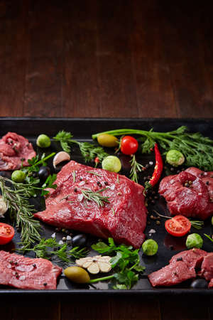 Flat lay of raw beefsteak with tomatoes, garlic, hot pepper, dill, parsley, rosemary and spicies on...