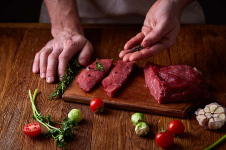 Preparation for dinner. Cooking, processing of meat. Strong professional man's hands spilling salt on raw beefsteak, selective focus, close-up. Self-confident chef on his work. Studio shot. Healthy eating dieting. Food background.の写真素材