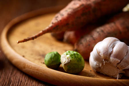 Colorful various of organic farm vegetables with fresh carrots, garlic, onion, brussel sprout on wooden plate over rustic background, top view, selective focus. Vegetable background. Dieting harvest. Seasoning veggies. Healthy eating concept.の写真素材