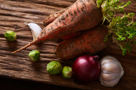 Organic farm vegetables with fresh carrots, garlic, onion, brussel sprout on flat piece of wood over rustic background, top view, selective focus. Vegetable background. Dieting harvest. Seasoning veggies. Healthy eating concept.の写真素材