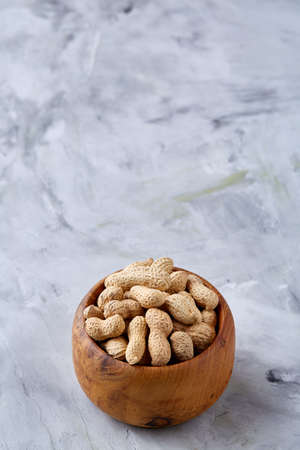 Unpeeled peanuts in wooden bowl over white textured background closeup, selective focus. Healthful and nutritious snack. Delicious ingredient for your every day cooking. Healthy lifestyle concept.の写真素材