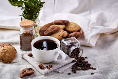 Breakfast still life with coffee cup on napkin, overturned jar with coffee beans, sweet cookies on...