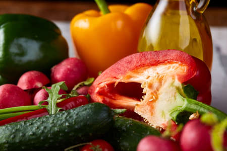 Still life of wooden plate with vegetables for a vegetarian salad on white textured background, close-up, selective focus. Cucumber, raddish, bell pepper and hot pepper served oil jar . Vegetable background. Food concept.の写真素材