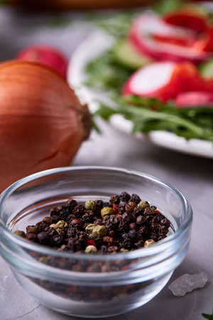 Glass bowl with dried allspice seeds in front of plate with fresh vegetable salad on white textured background, selective focus, vertical. Nesessary spice for every tasty dish. Crystal ingredient. Oraganic natural condiment. Food concept.の写真素材