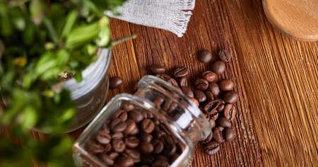 Side view of natural roasted coffee beans get out of overturned glass jar on wooden background, selective focus. Caffeinated composition. Stimulating beverage. Coffee beans background. Studio shot. Natural brewed drink.の写真素材