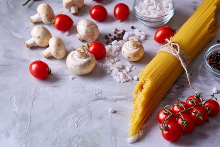Uncooked pasta, tomatoes, mushrooms and spice on white textured background, top view, close-up, selective focus. Some copy space. Preparation for cooking. Italian cuisine. Ingredients for perfect mediterranian meal. Food concept.の写真素材