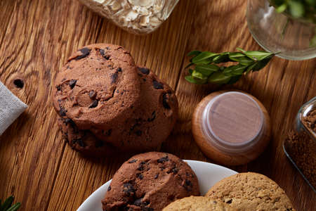 Side view of a plate of chocolate chip cookies on a white plate homespun tablecloth illuminated with...