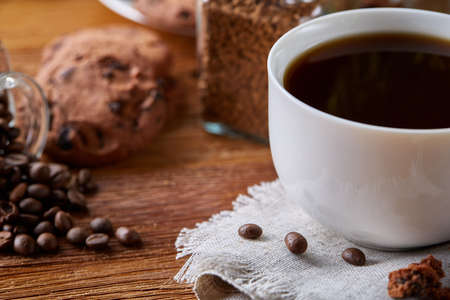 Breakfast still life with coffee cup on napkin, overturned jar with coffee beans, sweet cookies over rustic background, selective focus, close-up, top view. Delicious morning beverage. Time for calm and relax. Tasty dessert. Food concept.の写真素材