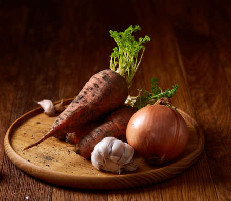Bundle of carrots with soil on wooden plate over rustic wooden background, side view, close-up, selective focus. Harvesting bunch. Fresh raw carotene. Unpeeled tasty roots. Healthy food background.の写真素材