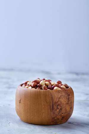 Mix of raw shelled peanuts in wooden plate isolated over white textured background, top view,...