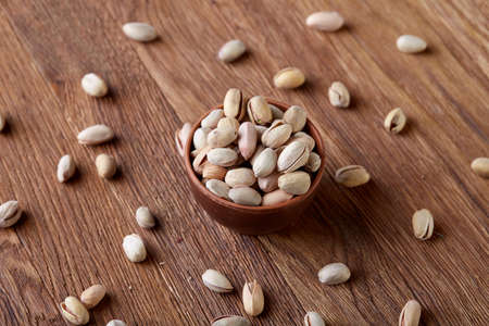 Salted pistachios on a wooden plate over rustic wooden background, top view, close-up, selective...