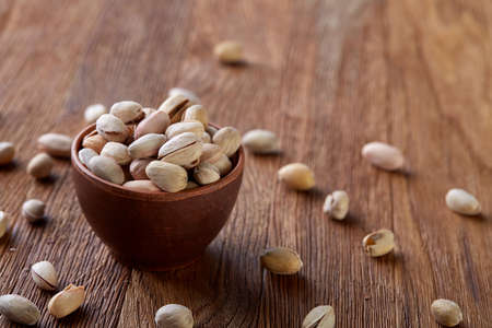 Salted pistachios on a wooden plate over rustic wooden background, top view, close-up, selective...
