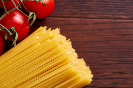 Uncooked pasta, tomatoes, mushrooms and two wooden spoon on rustic wooden background, top view, close-up, selective focus. Preparation for cooking. Italian cuisine. Ingredients for perfect mediterranian meal. Food concept.の写真素材