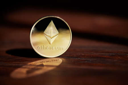 Golden ethereum blockchain cryptocurrency with its shadow on wooden table, close-up, macro, selective focus, shallow depth of field.Some copy space for your inscription. Electronic commerce. Cryptocurrency concept.の写真素材