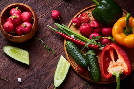 Fresh red radish in wooden bowl among plates with vegetables, ruccola and spicies on rustic wooden background, close-up, selective focus, shallow depth of field. Freshly gathered seasoning. Delicious appetizer. Summer garnish. Healthy food concept.の写真素材