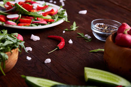 Creative fresh vegetable salad with ruccola, cucumber, tomatoes and raddish on white plate over wooden background, close-up, selective focus. Morning atmospheric lighting, fashionable trendy spot. Preparation for design creative menu. Food conceptの写真素材