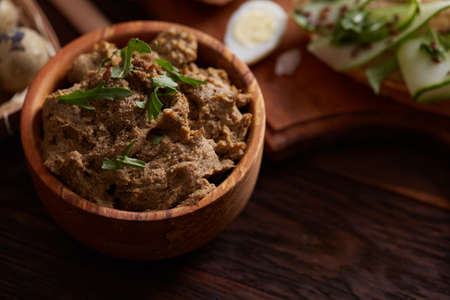 Paste from chicken liver in wooden bowl with vegetables on cutting board and quail eggs on wooden table, shallow depth of field, close-up. Gourmet buckish starter. Delicious excuisite appetizer. Sofisticated cuisine. Food concept.の写真素材