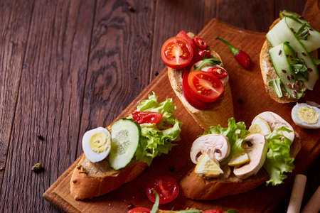 Breakfast sandwich with homemade paste, vegetables and fresh greenson wooden cutting board over rustic background, shallow depth of field, close-up. Delicious morning appetizer. Gourmet bruschetta. Healthy eating concept.の写真素材