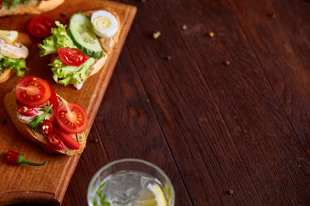 Breakfast sandwich with homemade paste, vegetables and fresh greenson wooden cutting board over rustic background, shallow depth of field, close-up. Delicious morning appetizer. Gourmet bruschetta. Healthy eating concept.の写真素材