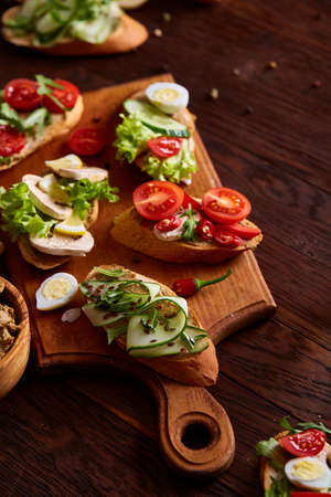 Breakfast sandwich with homemade paste, vegetables and fresh greenson wooden cutting board over rustic background, shallow depth of field, close-up. Delicious morning appetizer. Gourmet bruschetta. Healthy eating concept.の写真素材