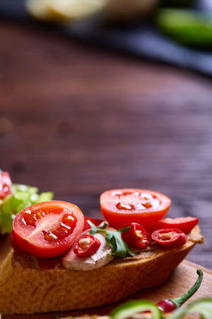 Breakfast sandwich with homemade paste, vegetables and fresh greenson wooden cutting board over rustic background, shallow depth of field, close-up. Delicious morning appetizer. Gourmet bruschetta. Healthy eating concept.の写真素材