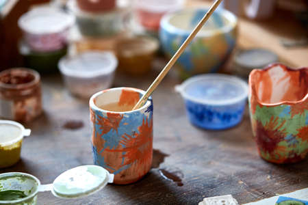 Close-up of various paint mugs and brushes in holder on worktop, selective focus, side view.