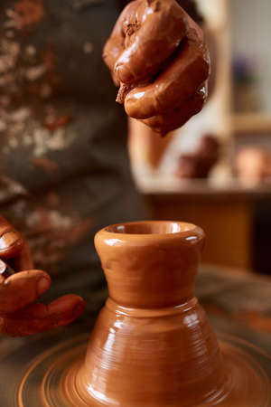 Close-up hands of a male potter in apron molds bowl from clay, selective focusの写真素材