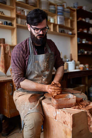 Portrait of a male potter in apron molds bowl from clay, selective focus, close-upの写真素材