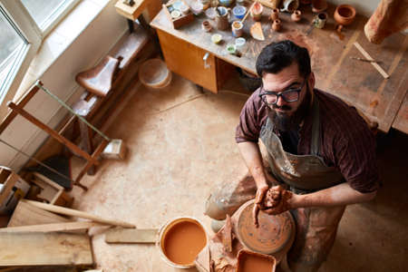 Portrait of a male potter in apron molds bowl from clay, selective focus, close-up