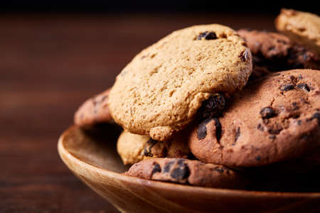 Side view of chocolate chip cookies on a wooden plate over rustic background illuminated with natural light, close-up, selective focus. Some copy space. Tasty homemade snack. Delicious pastry. Yummy caloric biscuits. Food concept.の写真素材