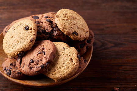 Side view of chocolate chip cookies on a wooden plate over rustic background illuminated with...