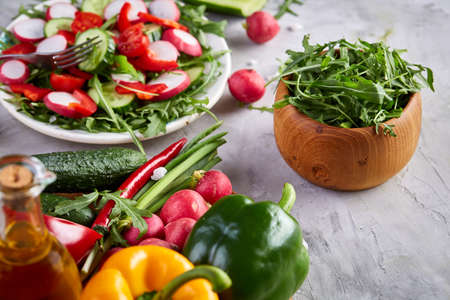 Creative fresh vegetable salad with ruccola, cucumber, tomatoes and raddish on white plate over textured background, close-up, selective focus. Morning atmospheric lighting, fashionable trendy spot. Preparation for design creative menu. Food conceptの写真素材