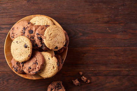 Side view of chocolate chip cookies on a wooden plate over rustic background illuminated with natural light, close-up, selective focus. Some copy space. Tasty homemade snack. Delicious pastry. Yummy caloric biscuits. Food concept.の写真素材