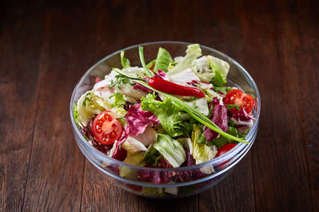 Fresh vegetable salad and ripe veggies on cutting board over wooden background, close up, selective focusの写真素材