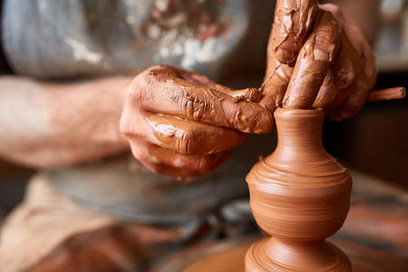 Close-up hands of a male potter in apron making a vase from clay, selective focusの写真素材