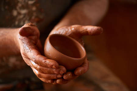 Close-up hands of a male potter in apron making a vase from clay, selective focusの写真素材