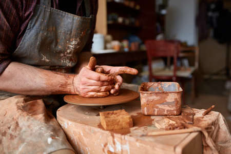 Portrait of a male potter in apron molds bowl from clay, selective focus, close-up