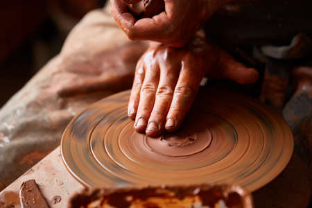 Close-up hands of a male potter in apron making a vase from clay, selective focusの写真素材