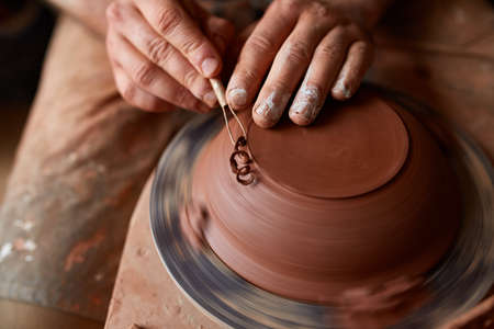 Close-up hands of a male potter in apron making a vase from clay, selective focus
