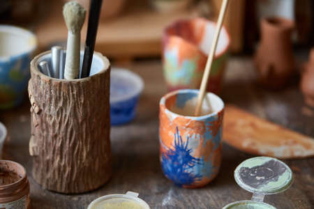 Close-up of various paint mugs and brushes in holder on worktop, selective focus, side view.