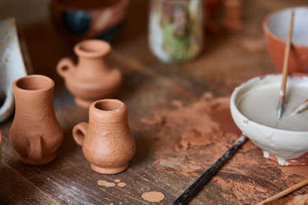 Close-up of various paint mugs and brushes in holder on worktop, selective focus, side view.