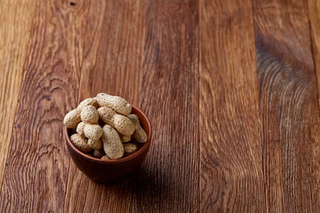 Unpeeled peanuts in wooden bowl over rustic wooden background closeup, selective focusの写真素材