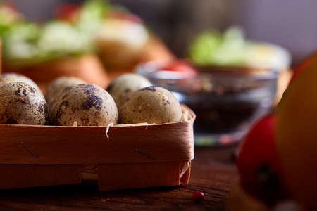 Fresh eggs of a quail with greens and vegetables on wooden table, selective focus, close-up