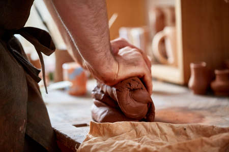Adult male potter master modeling the clay plate on potters wheel. Top view, closeup, hands only.