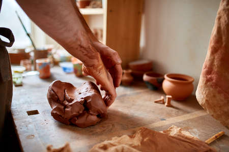 Adult male potter master modeling the clay plate on potters wheel. Top view, closeup, hands only.
