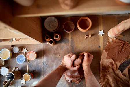 Adult male potter master modeling the clay plate on potters wheel. Top view, closeup, hands only.の写真素材