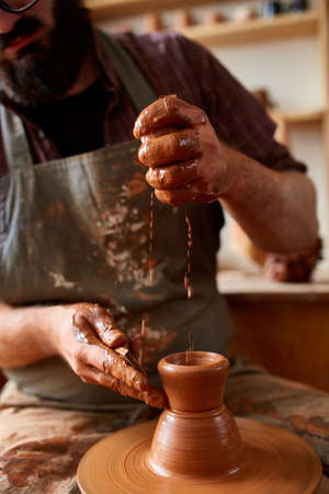 Portrait of a male potter in apron molds bowl from clay, selective focus, close-upの写真素材
