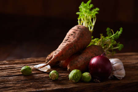 Bundle of carrots with soil over rustic wooden background, side view, close-up, selective focus, low...