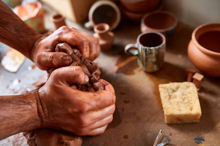 Adult male potter master modeling the clay plate on potters wheel. Top view, closeup, hands only.の写真素材
